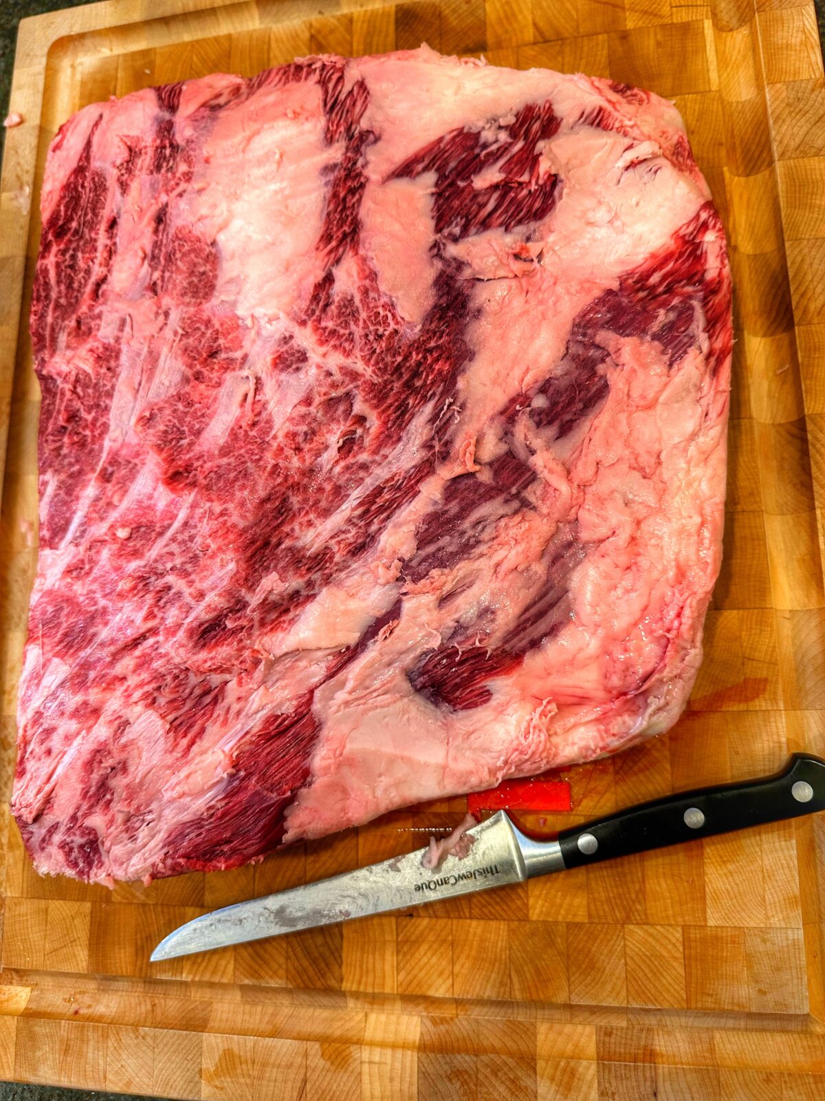 Trimmed beef plate ribs and a knife on a cutting board.