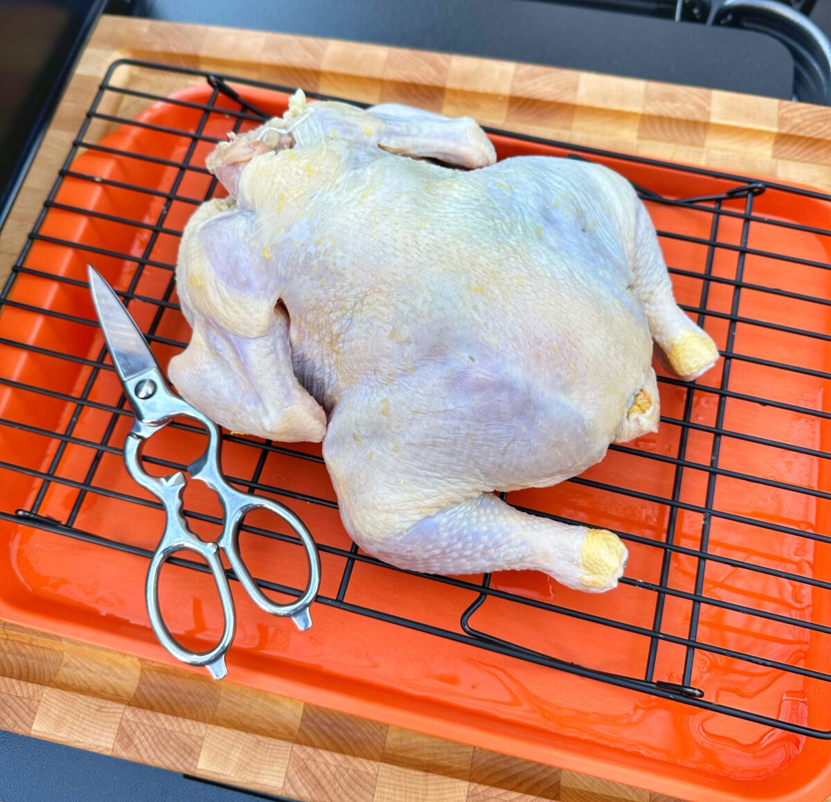 Whole chicken on a metal rack before being cut.