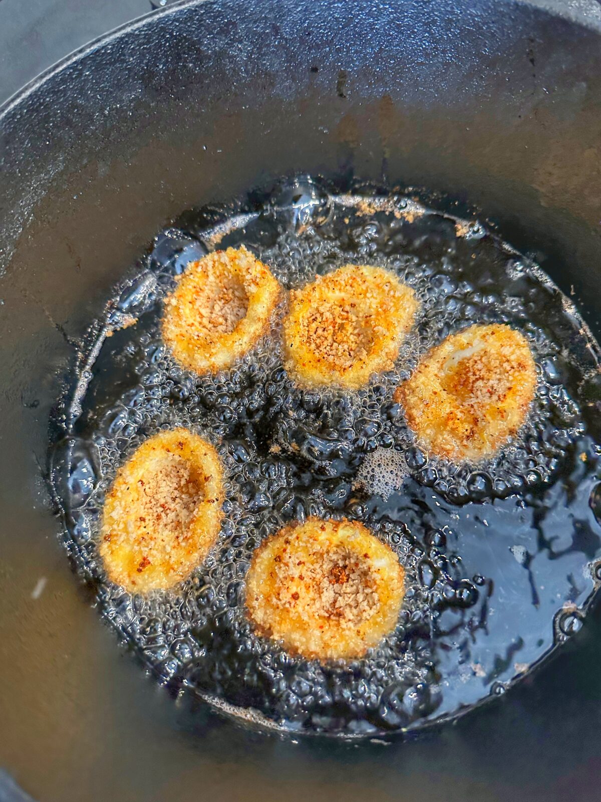 Five egg halves frying in a cast iron pot.