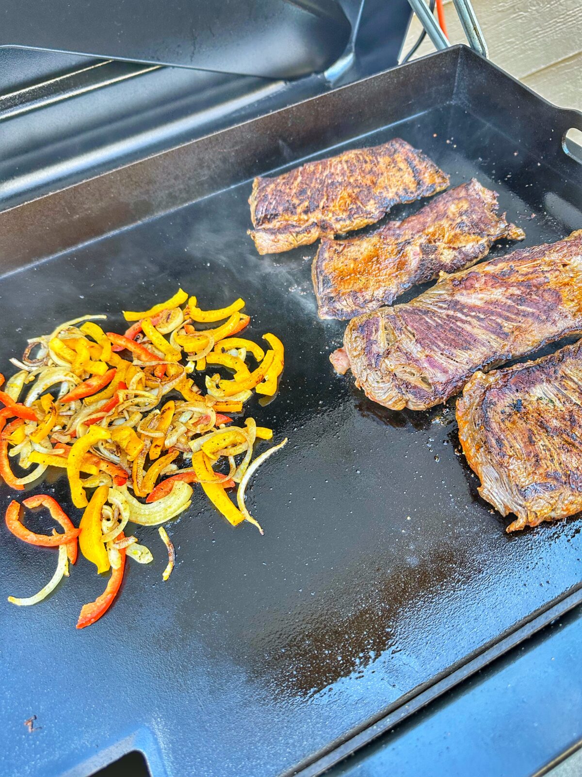Skirt steak and peppers cooking on the griddle.