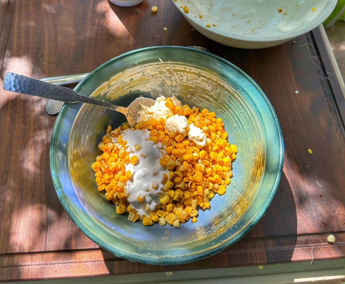A green bowl with griddled corn and sour cream.