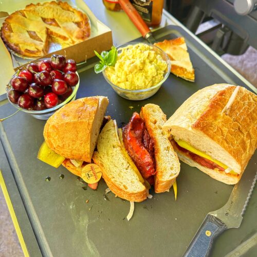 A country-style pork rib sandwich, fresh cherries, potato salad and peach pie on a board.