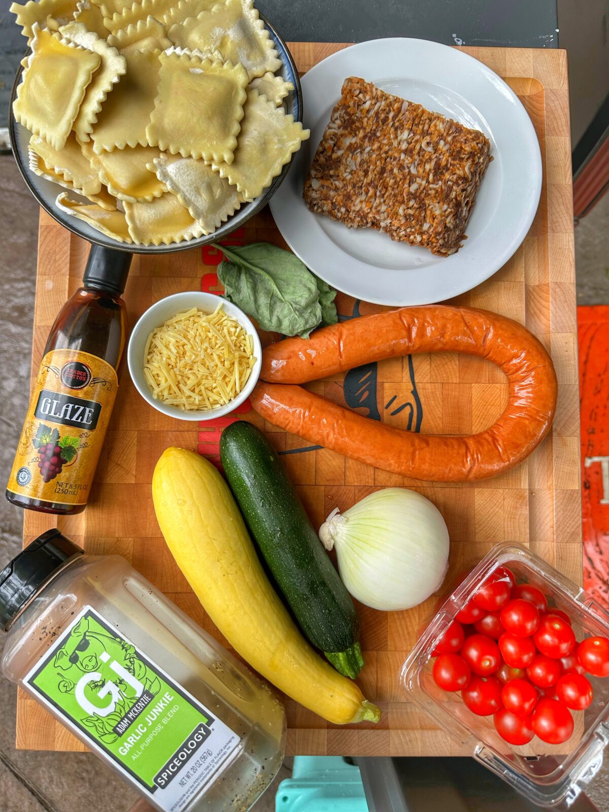 Ravioli, sausages, vegetables, and other ingredients on a cutting board.