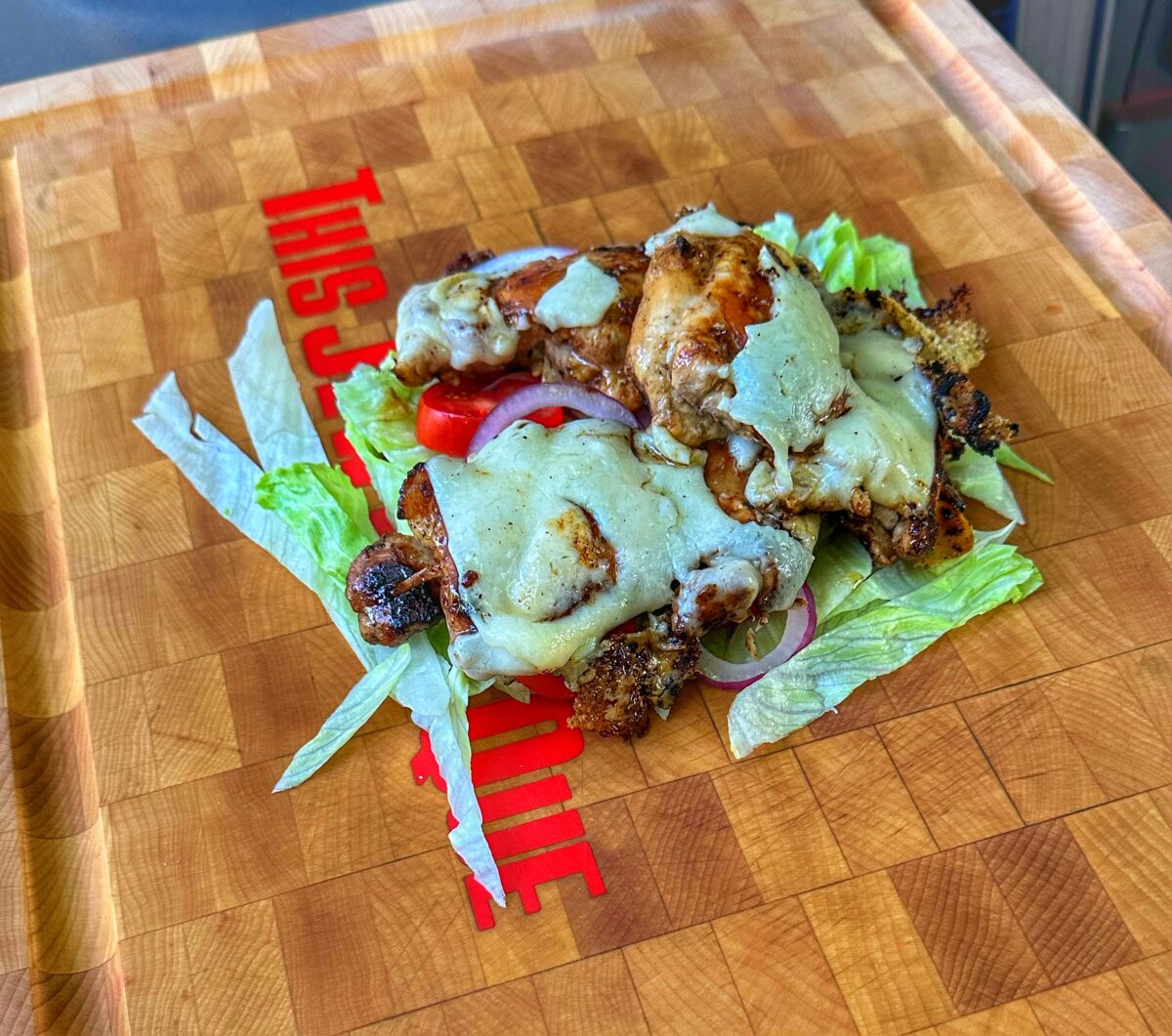 Grilled chicken thighs topped with cheese on a cutting board.