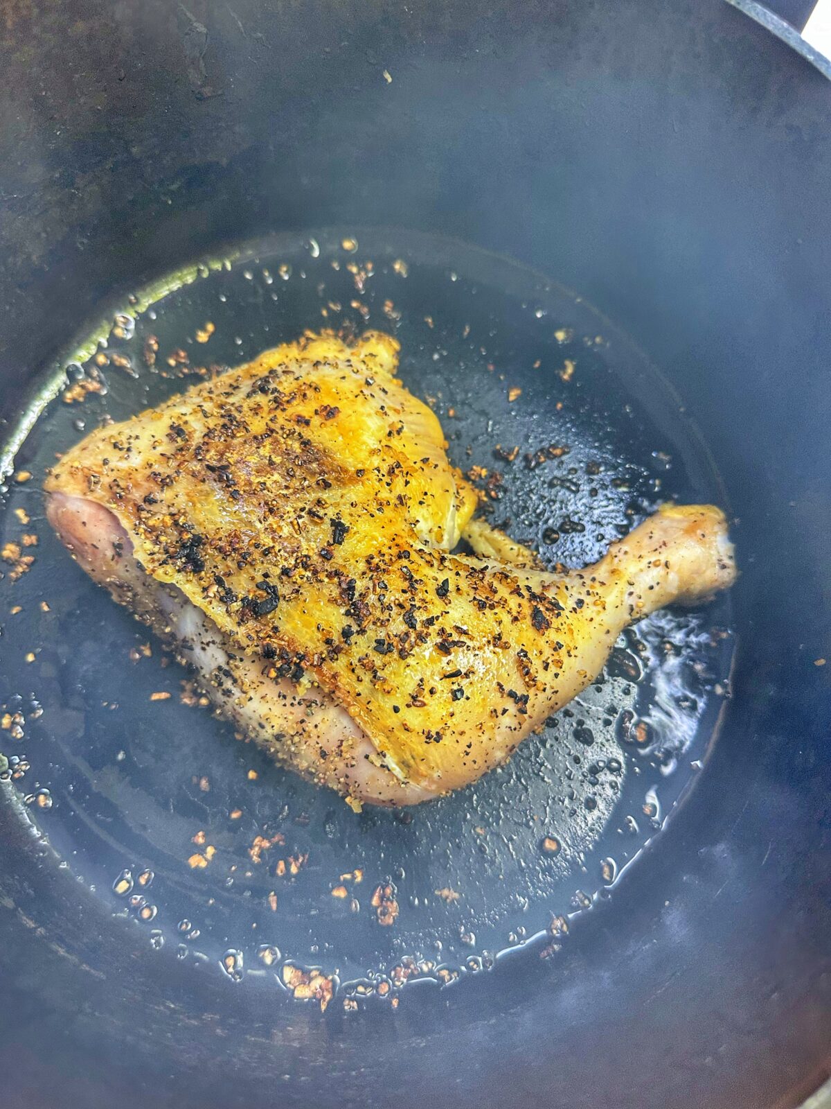 A chicken quarter searing in a cast iron dutch oven.