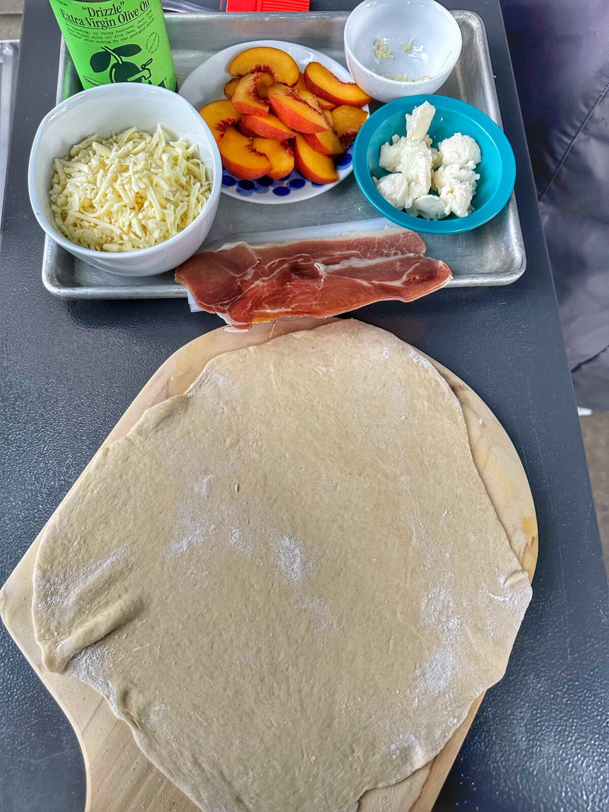 Ingredients for Serrano ham and peach pizza on a tray with a stretched pizza dough.