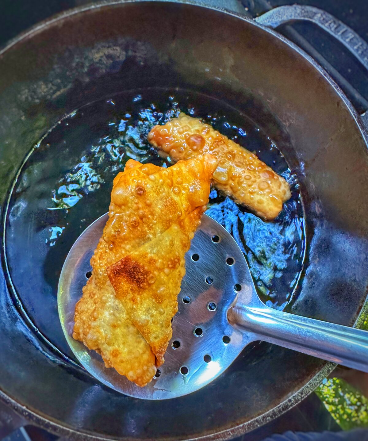 Two golden southwest egg rolls frying in a cast iron pan.