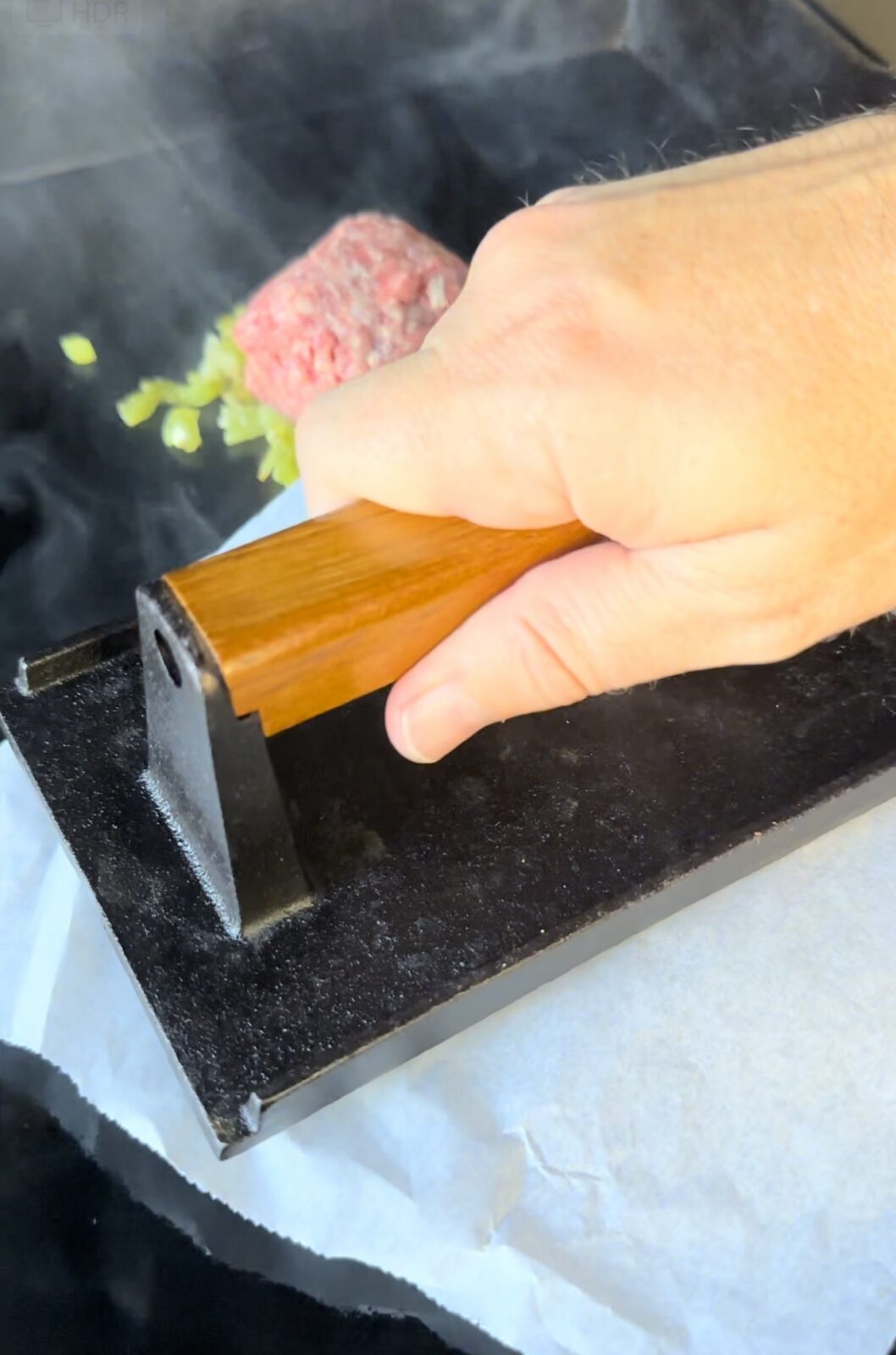 A hand pressing smash burgers on the griddle.