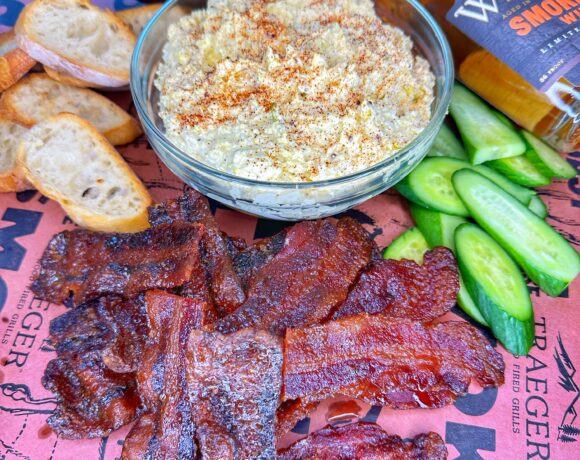 A bowl of smoked deviled egg dip with candied bacon strips.