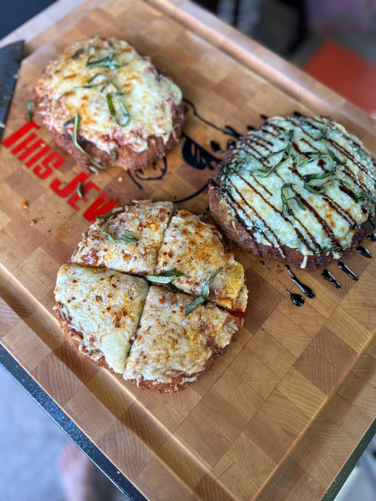 Three chicken parm pizzas on a cutting board.