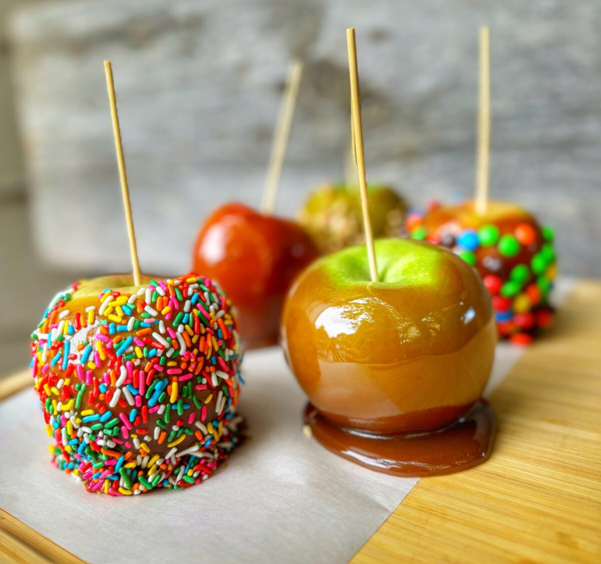 Four shiny smoked caramel apples on a cutting board.