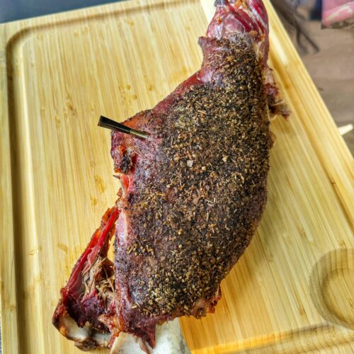 A whole goat leg, smoked, on a cutting board.