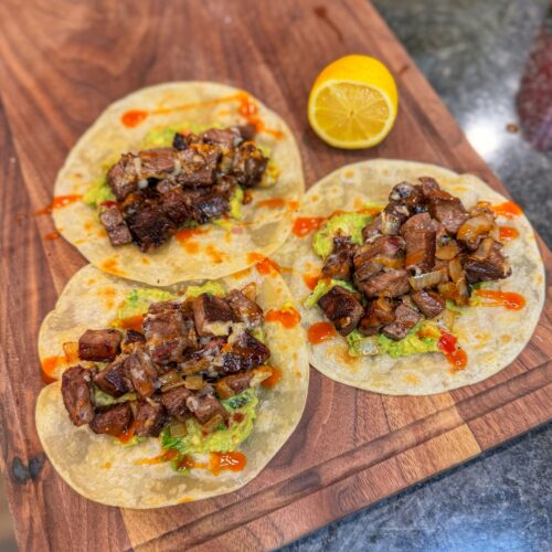 A trio of prime rib tacos on a cutting board.
