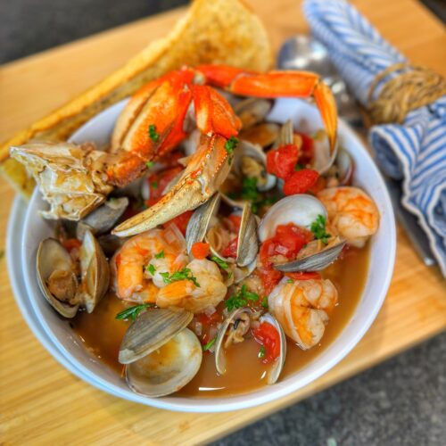 A bowl of cioppino on a cutting board.