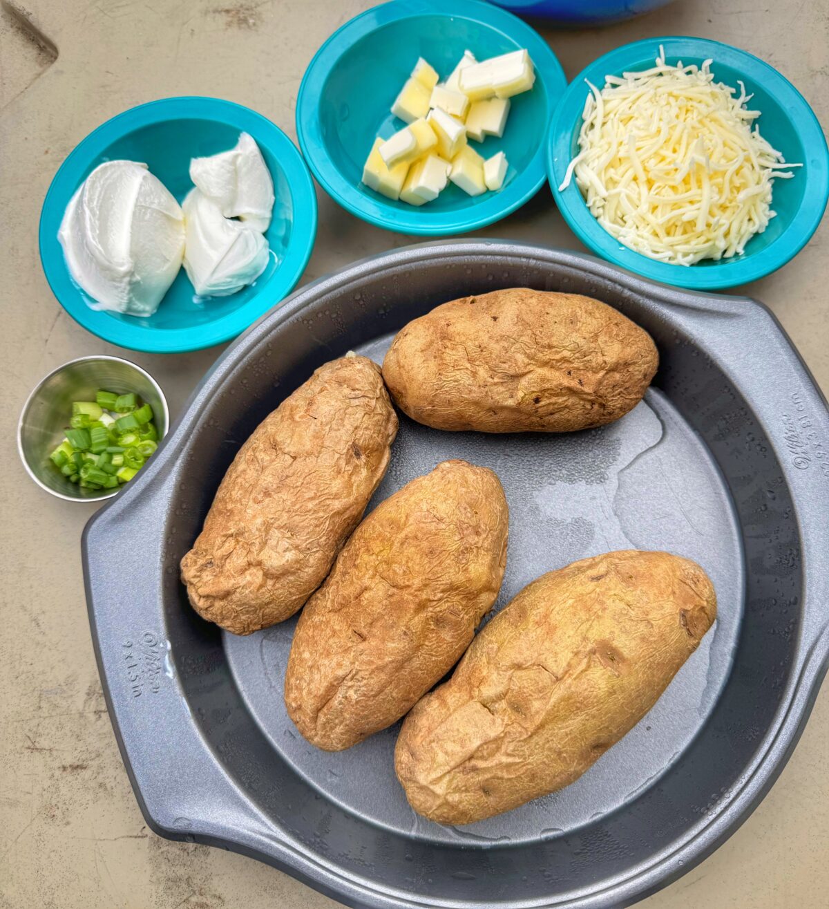 Ingredients for petite twice baked potatoes, including baked russet potatoes, sour cream, butter, shredded cheese, and chopped scallions.