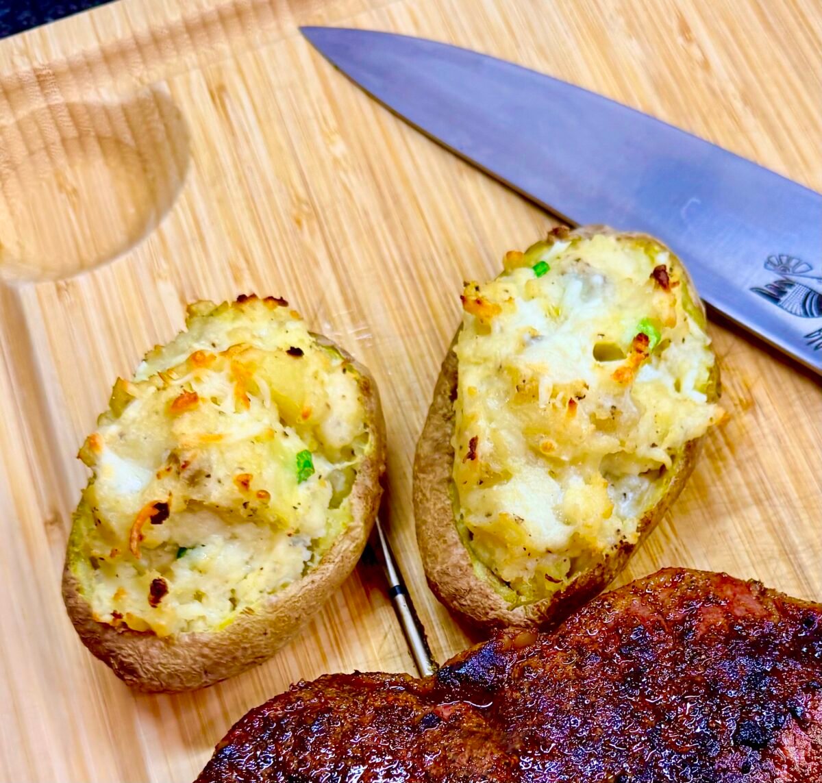Golden, crispy petite twice baked potatoes with a creamy, cheesy filling, served alongside a juicy, grilled steak on a wooden cutting board.