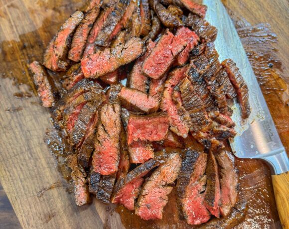 Juicy, medium-rare citrus-marinated skirt steak sliced against the grain on a wooden cutting board with a sharp knife.