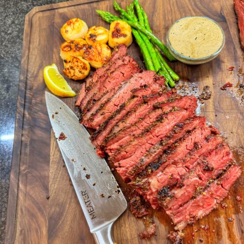 Reverse-seared Bavette steak sliced on a wooden cutting board, served with seared scallops, asparagus, and whiskey cream sauce.