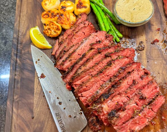 Reverse-seared Bavette steak sliced on a wooden cutting board, served with seared scallops, asparagus, and whiskey cream sauce.