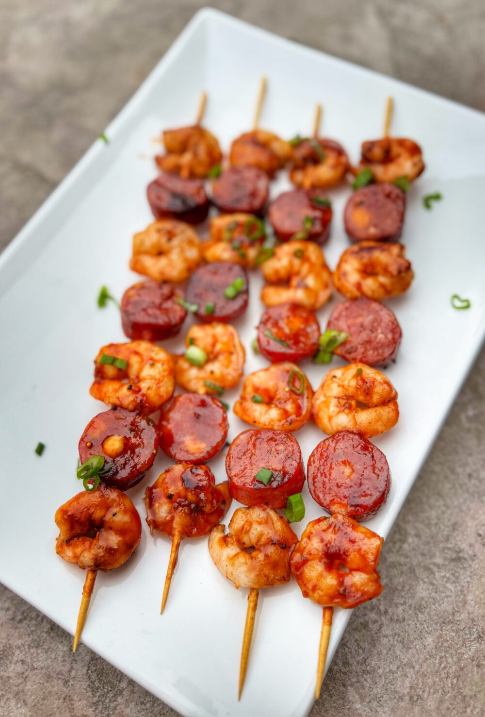 Cooked shrimp and sausage skewers plated on a white rectangular serving dish.