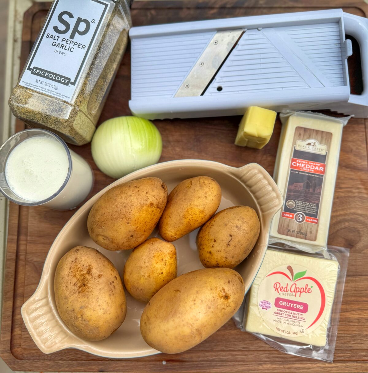 Ingredients for Traeger scalloped potatoes including gold potatoes, onion, cream, butter, cheese, and a mandoline slicer.