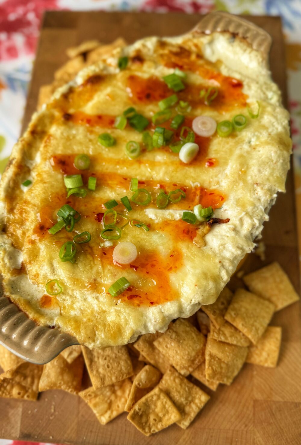 Baked crab rangoon dip topped with scallions and sweet chili sauce, served with wonton chips.