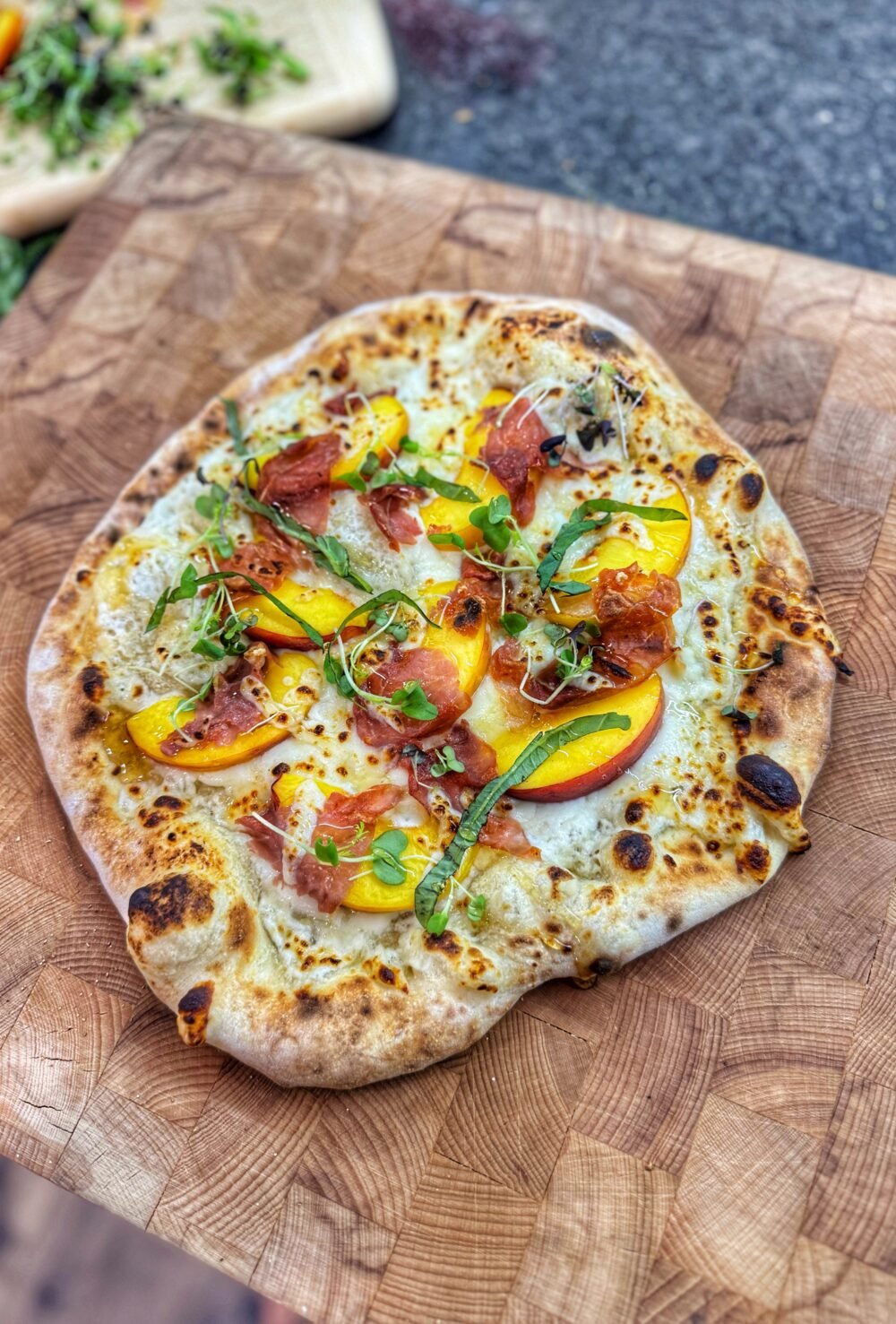 Golden brown pizza topped with peaches, prosciutto, melted cheese, and microgreens.
