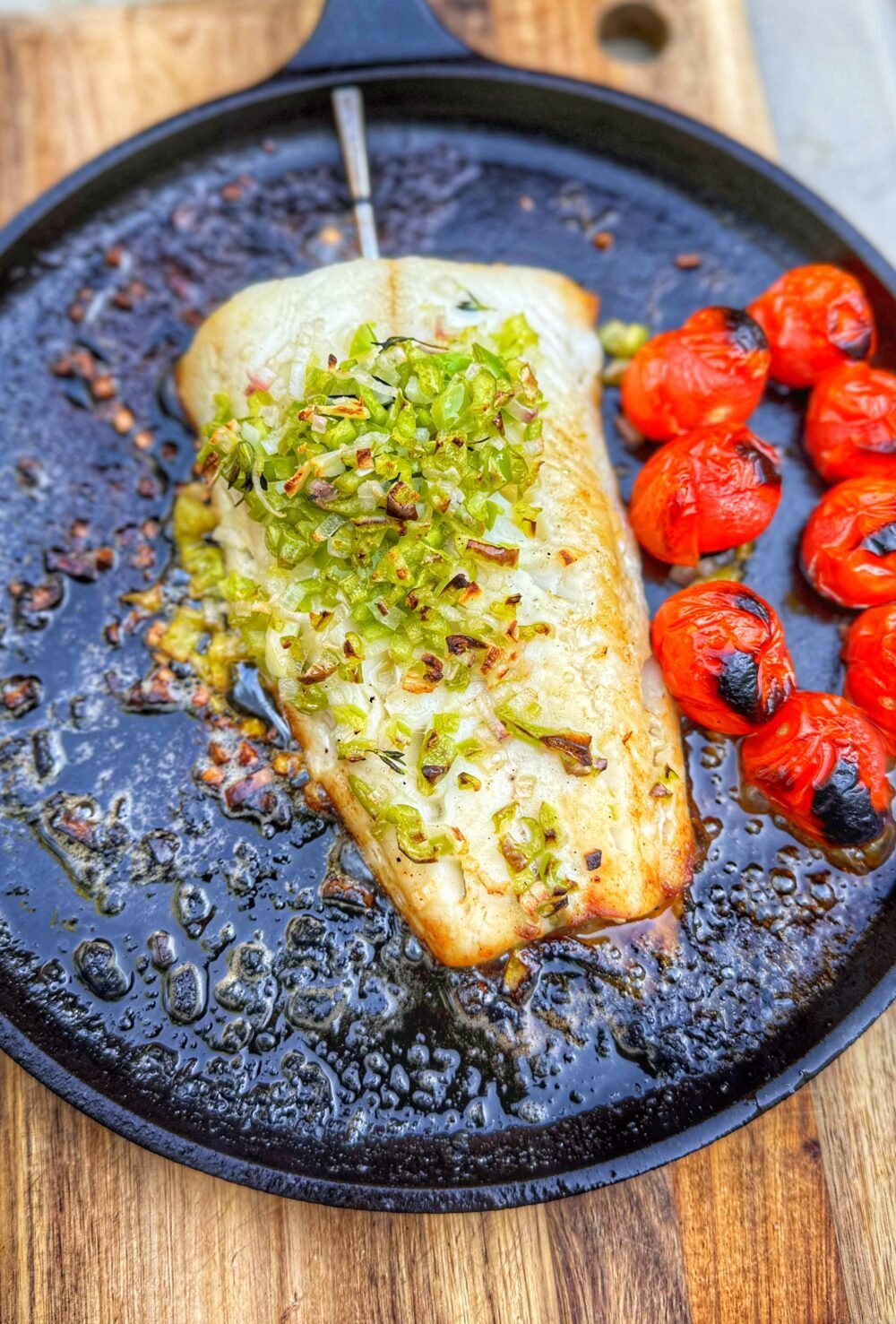 Wood fired sablefish fillet topped with Hatch chile beurre blanc and charred cherry tomatoes in cast iron pan.