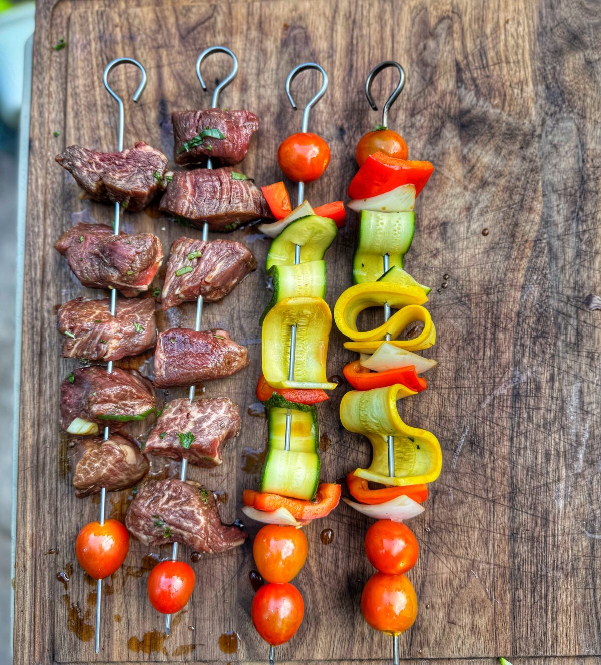 Assembled raw skewers with steak, cherry tomatoes, onions, peppers, and squash ribbons.