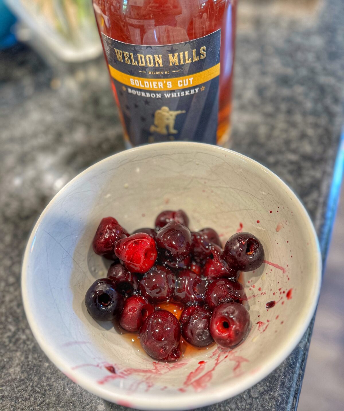 Bowl of cherries with bourbon bottle in the background.