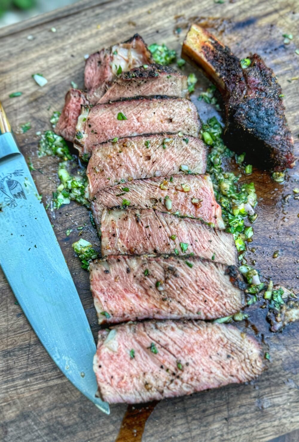 Sliced ribeye steak on a cutting board with garlic herb board sauce and a chef’s knife.