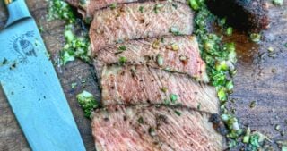 Sliced ribeye steak on a cutting board with garlic herb board sauce and a chef’s knife.