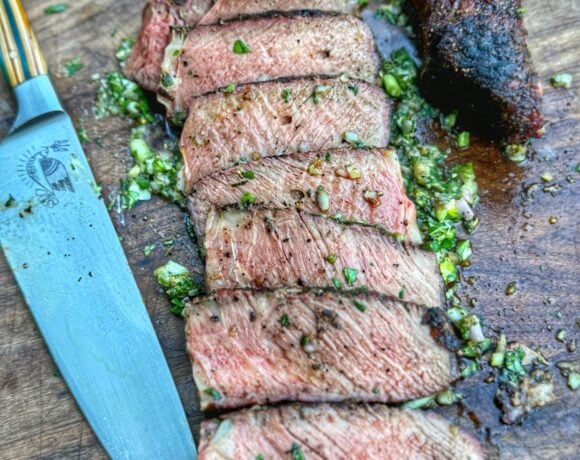 Sliced ribeye steak on a cutting board with garlic herb board sauce and a chef’s knife.