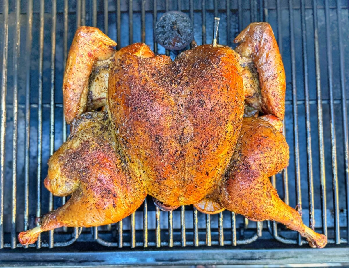 Spatchcock turkey with golden brown skin cooking on grill grates with thermometer inserted.