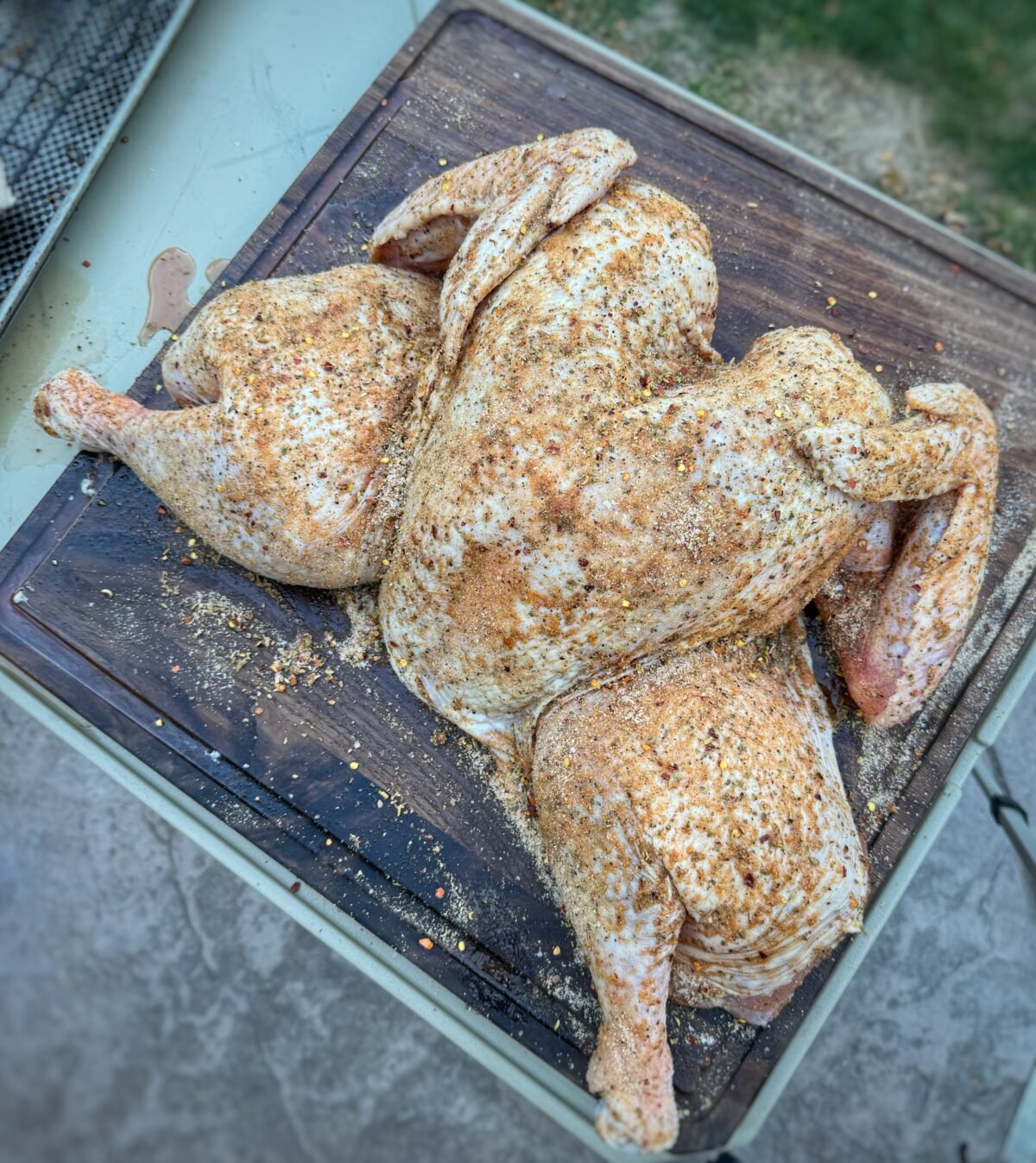 Raw spatchcock turkey covered with dry rub on a wooden cutting board.