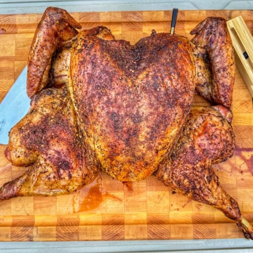 Fully cooked spatchcock turkey resting on a wooden cutting board with carving knife and thermometer.