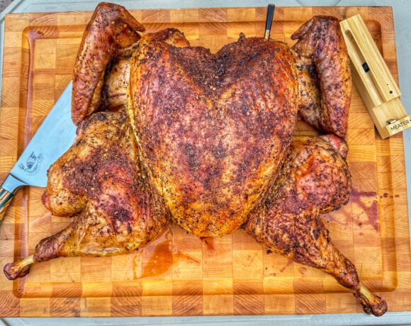 Fully cooked spatchcock turkey resting on a wooden cutting board with carving knife and thermometer.