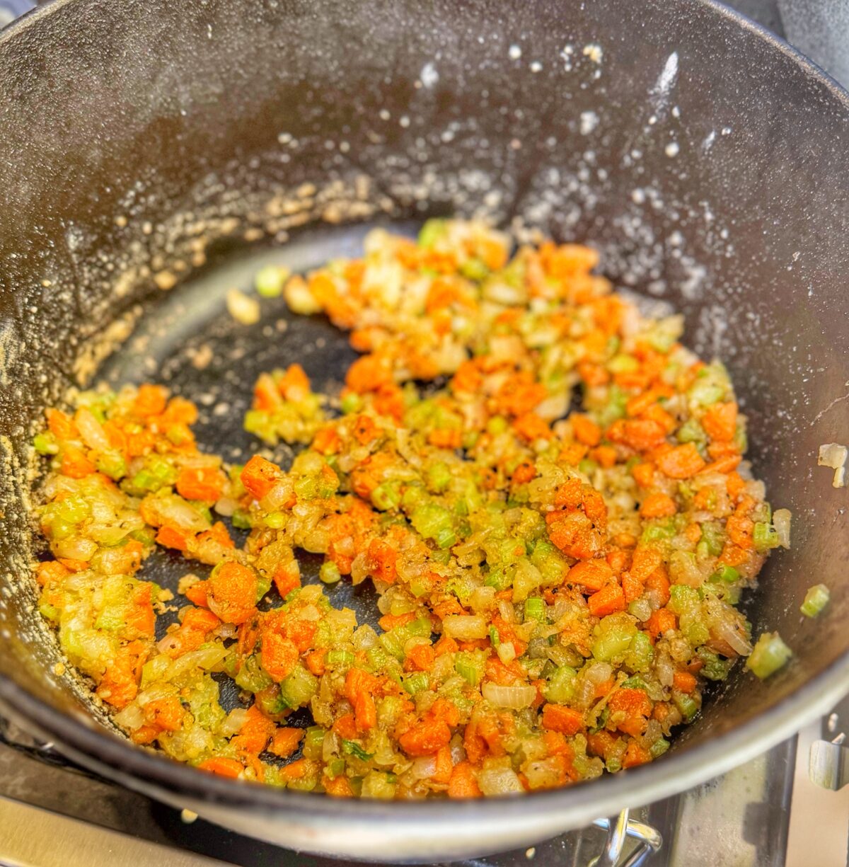 Vegetables sautéing in butter inside a cast iron pot on a Weber Spirit grill side burner.