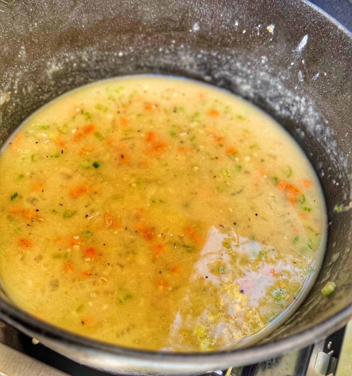 A pot of beer cheese soup simmering on an outdoor grill side burner.