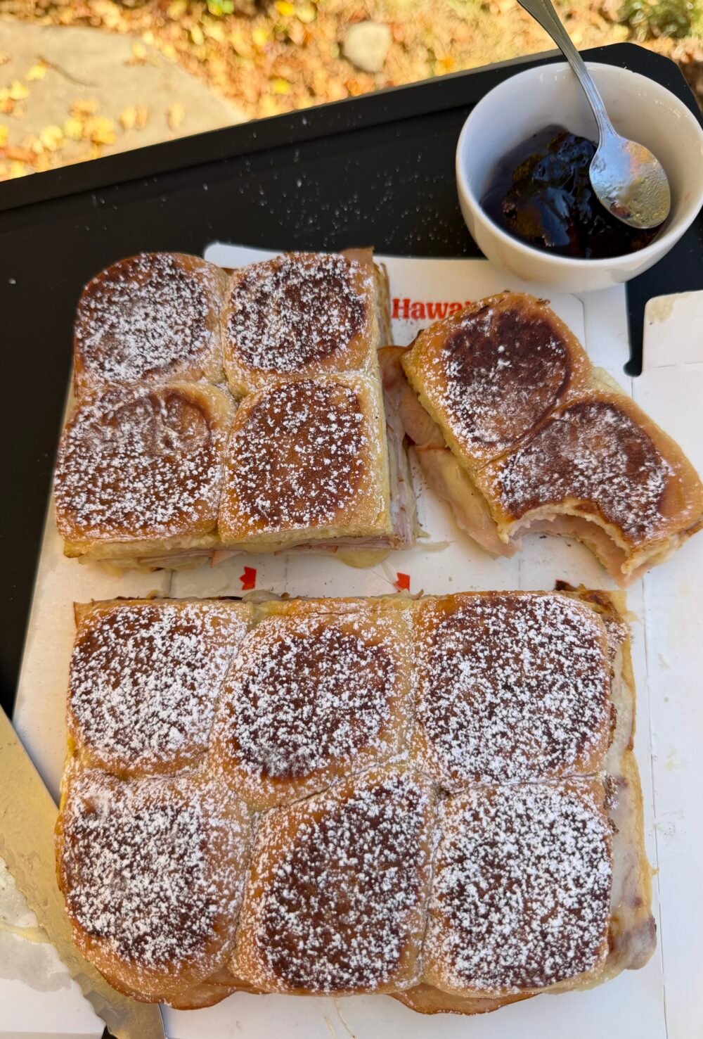 Monte Cristo sliders cut into sections on a tray, dusted with powdered sugar, served with grape jelly in a bowl.