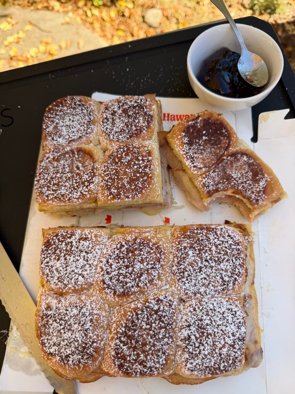 Monte Cristo sliders cut into sections on a tray, dusted with powdered sugar, served with grape jelly in a bowl.