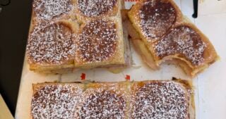 Monte Cristo sliders cut into sections on a tray, dusted with powdered sugar, served with grape jelly in a bowl.