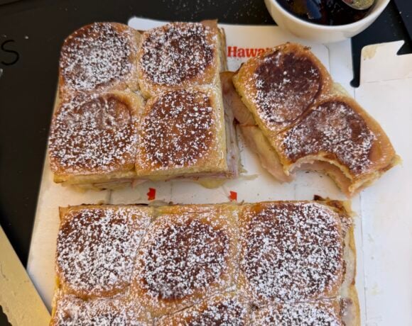 Monte Cristo sliders cut into sections on a tray, dusted with powdered sugar, served with grape jelly in a bowl.