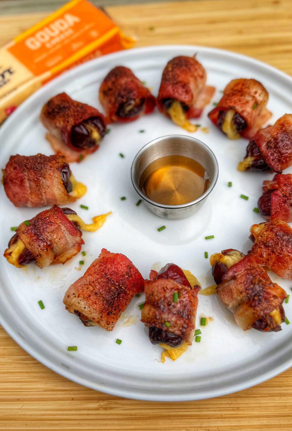 Overhead view of a platter of bacon-wrapped dates stuffed with Cabot Gouda, arranged neatly for serving.