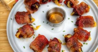 Overhead view of a platter of bacon-wrapped dates stuffed with Cabot Gouda, arranged neatly for serving.