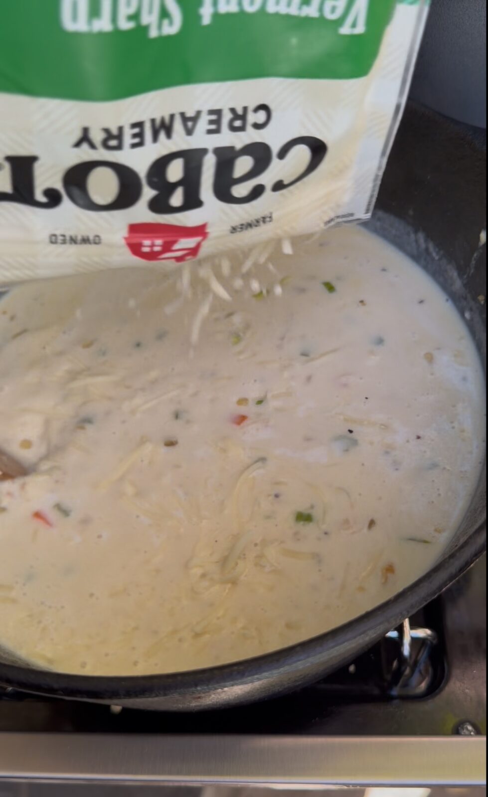 A bag of Cabot Vermont Sharp shredded cheddar being poured into a pot of soup.