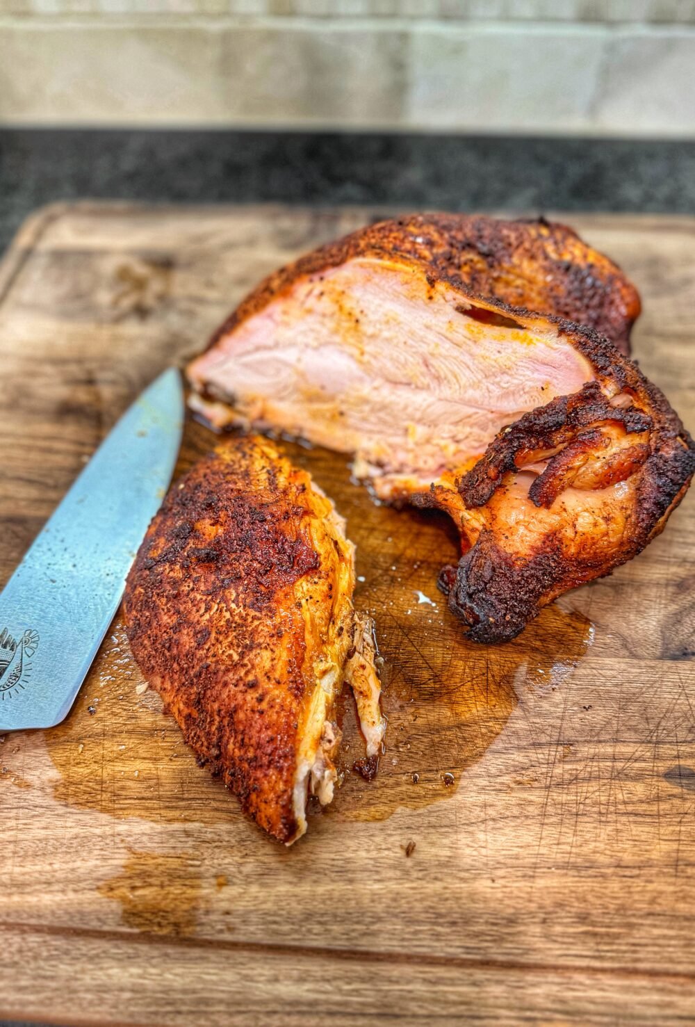 Sliced smoked turkey breast on a wooden cutting board, showing juicy interior meat with a browned, seasoned crust, alongside a chef’s knife.