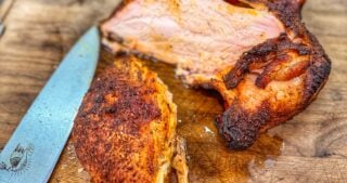 Sliced smoked turkey breast on a wooden cutting board, showing juicy interior meat with a browned, seasoned crust, alongside a chef’s knife.