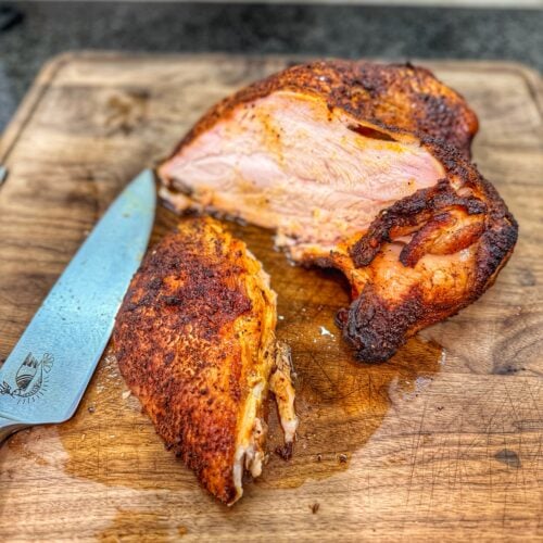 Sliced smoked turkey breast on a wooden cutting board, showing juicy interior meat with a browned, seasoned crust, alongside a chef’s knife.