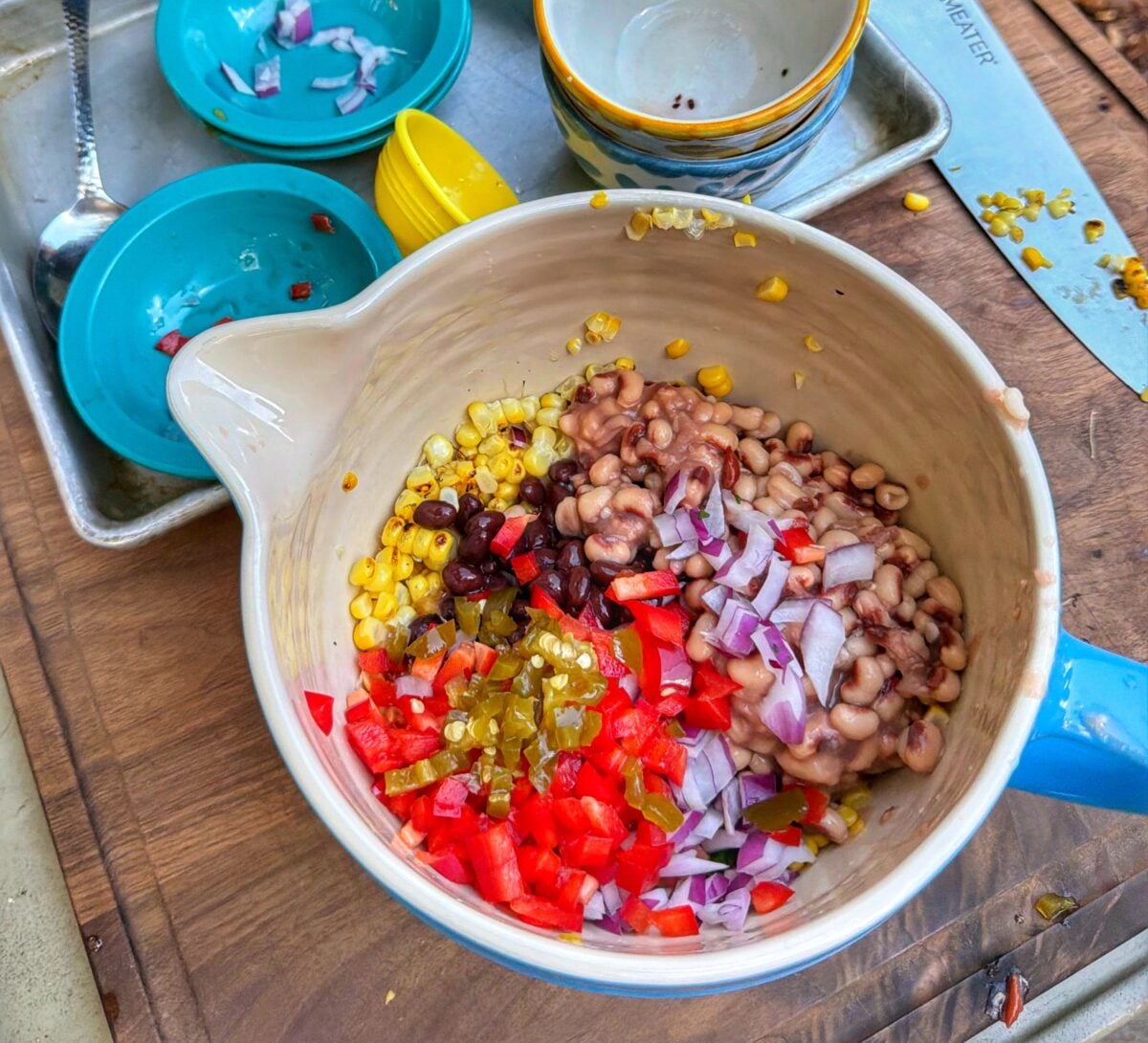 Mixing bowl with black-eyed peas, corn, black beans, diced onion, diced red pepper, and chopped jalapeños